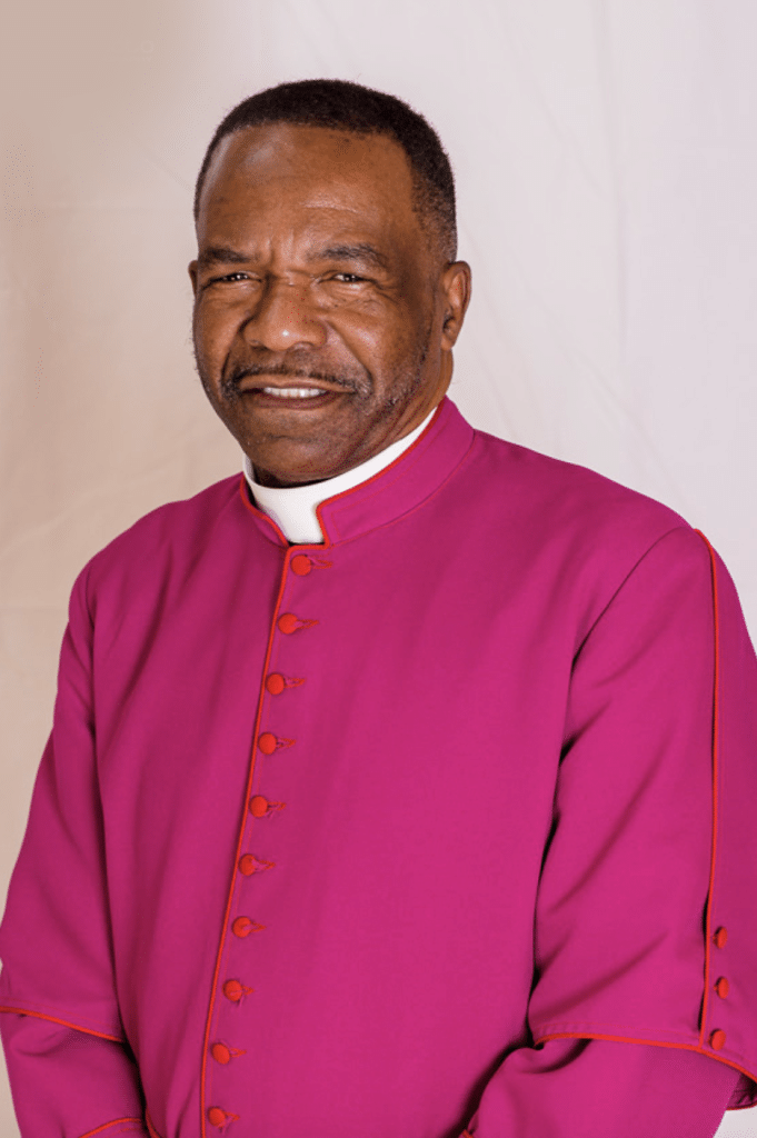 A man in a pink apostolic priest's robe posing for a photo at church.