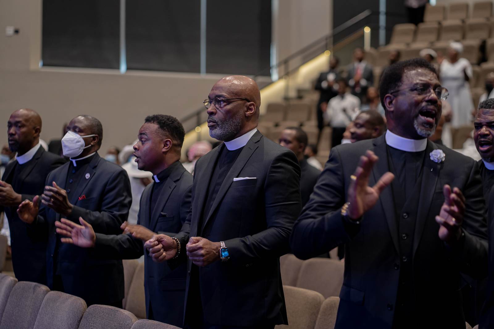 A group of apostolic men in suits clapping in a church.